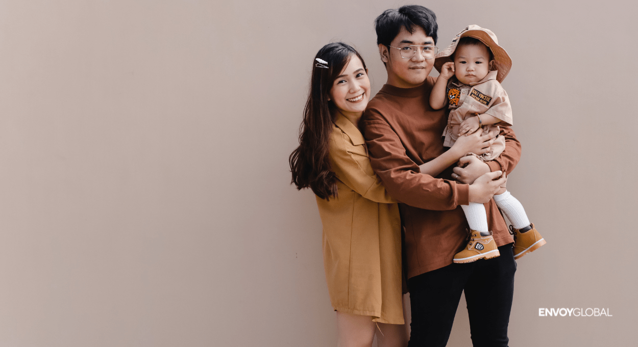 Image of a family holding a child smiling at the camera with the Envoy Global logo in the bottom right hand corner.